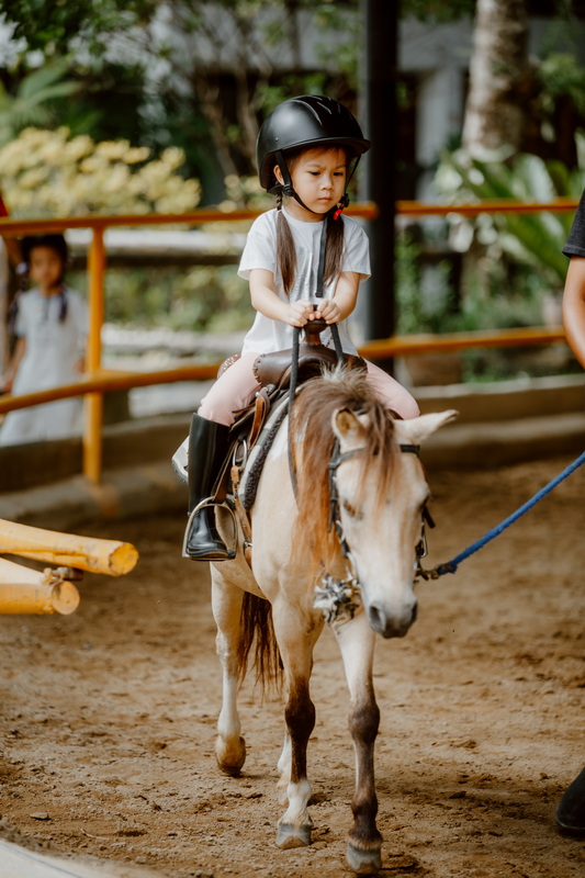 Young girl riding a small horse wearing a helmet inside an indoor arena at Horse Riding Chiang Mai.