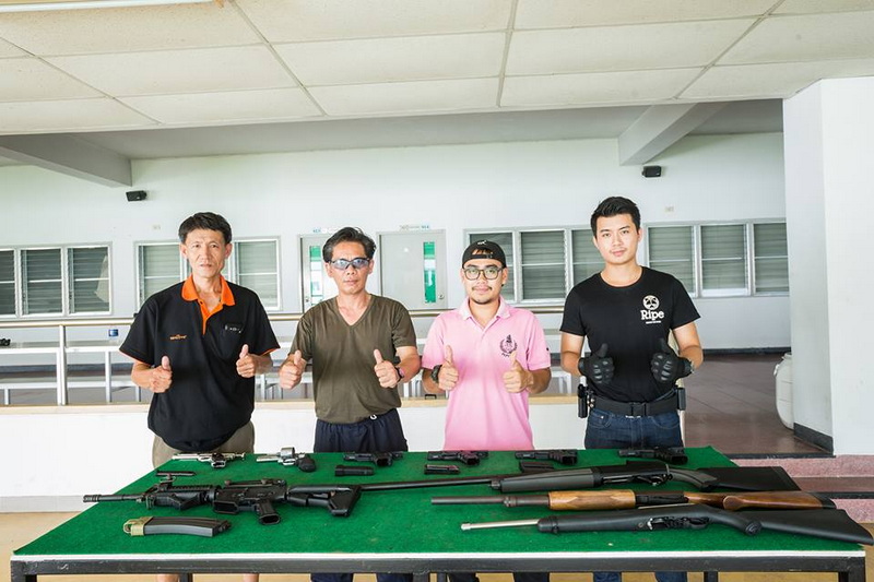 Group of four people indoors with guns displayed on table behind them at Chiang Mai Shooting Range.