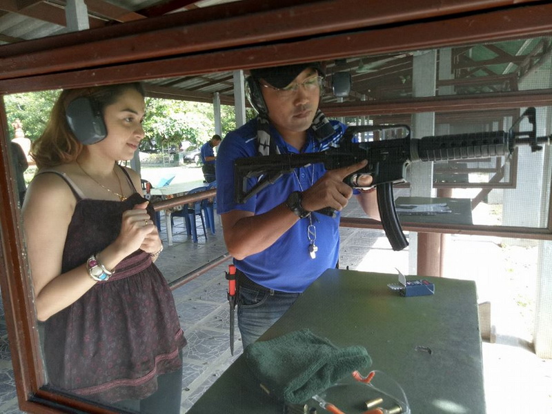 People Shooting at Range at Chiang Mai Shooting Club A woman and a man aiming rifles at a shooting range enclosed in glass at Chiang Mai Shooting Club.
