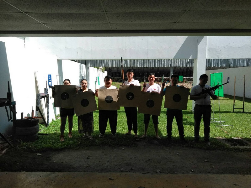 Seven people standing inside with shooting targets and a person holding a rifle at Chiang Mai Shooting Range.