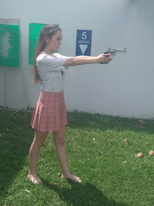 Woman with Revolver Aiming Outdoors at Chiang Mai Shooting Club Young woman in white shirt holding a revolver outdoors near a target sign at Chiang Mai Shooting Club.