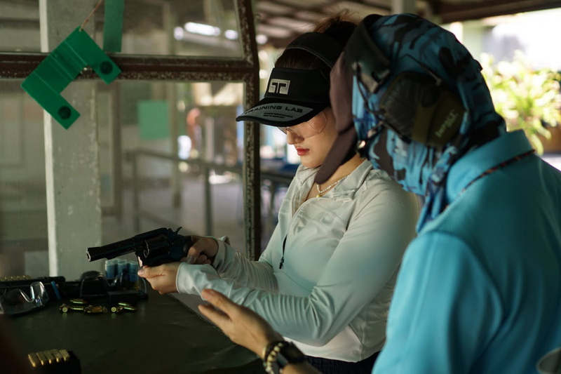Woman handling a handgun with a trainer at a shooting range indoors at Chiang Mai Shooting Club.