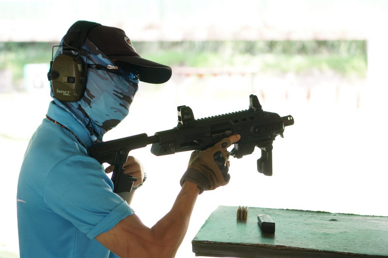 Person aiming a rifle indoors with ear protection and gloves at Chiang Mai Shooting Club.