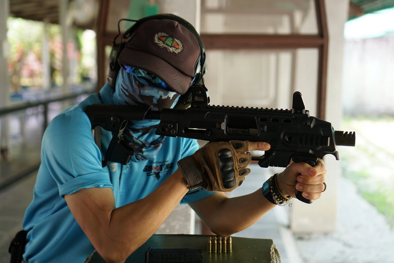 Person aiming a rifle at an indoor shooting range wearing gloves and face covering at Chiang Mai Shooting Range.