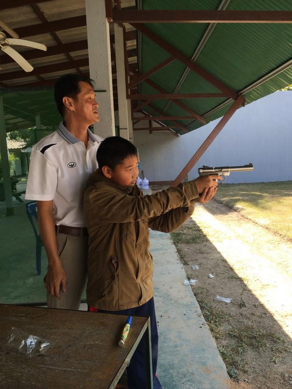 Boy aiming a pistol with instructor observing at shooting range at Chiang Mai Shooting Range.