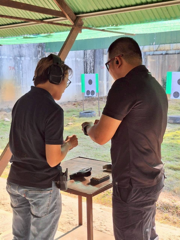 Two individuals with ear protection examining guns at a shooting range at Chiang Mai Shooting Club.