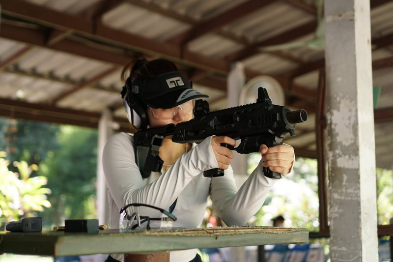 Woman in protective gear aiming a rifle at a shooting range outdoors at Chiang Mai Shooting Club.