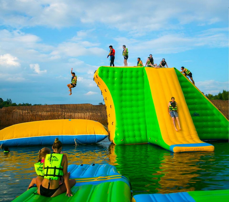Inflatable Water Play Area at Grand Canyon Chiang Mai Children enjoying an inflatable water slide and boat by a lake under a blue sky at Grand Canyon Chiang Mai.