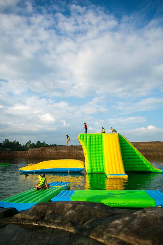 People enjoying inflatable water slides on a river under a blue sky with clouds at Grand Canyon Chiang Mai.