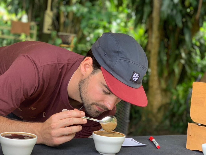 Man tasting coffee outdoors with lush green trees and foliage in background at Coffee Farm Tour Chiang Mai.