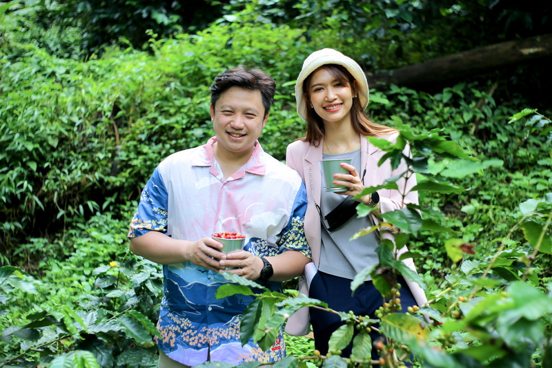 Coffee Garden Visitors at Chiang Mai Coffee Farm Tour Two smiling individuals holding coffee cups among vibrant coffee plants at Chiang Mai Coffee Farm Tour.
