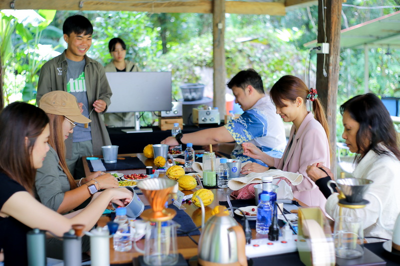 People gather around a table with coffee gear inside a green shelter at Coffee Farm Tour Chiang Mai.