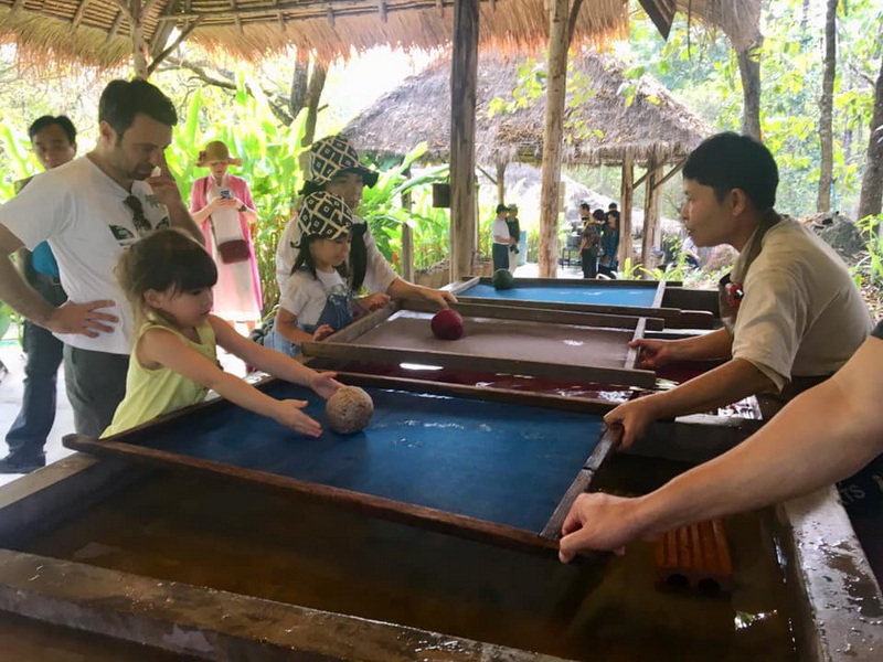 Tropical Ball Game Experience at Elephant Poopoo Paper Park Children and adults playing a ball game under shade in a lush tropical environment at Elephant Poopoo Paper Park.