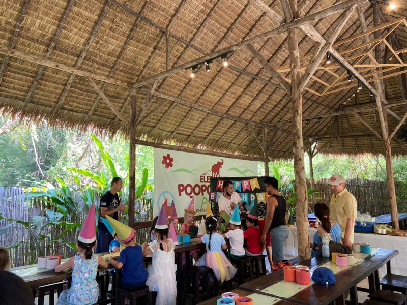 Children's Birthday Celebration at Elephant Poopoopaper Park Kids celebrating a birthday with party hats inside a thatched pavilion surrounded by greenery at Elephant Poopoopaper Park.