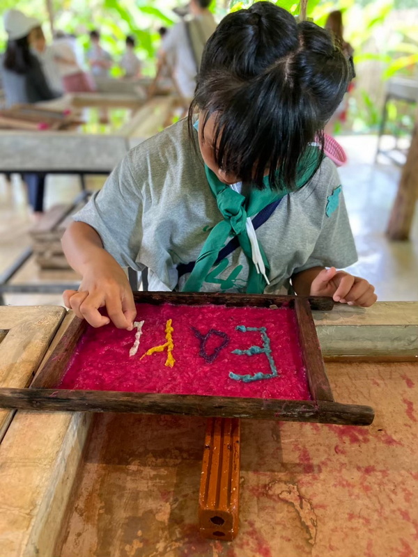 Scout Activity with Colored Traces at Elephant Poopoopaper Park Person in scout uniform tracing colorful objects on a pink textured surface indoors at Elephant Poopoopaper Park.