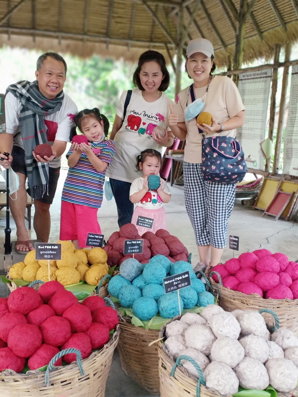 Family holding colorful handmade paper balls inside a thatched-roof shop at Elephant Poopoopaper Park.