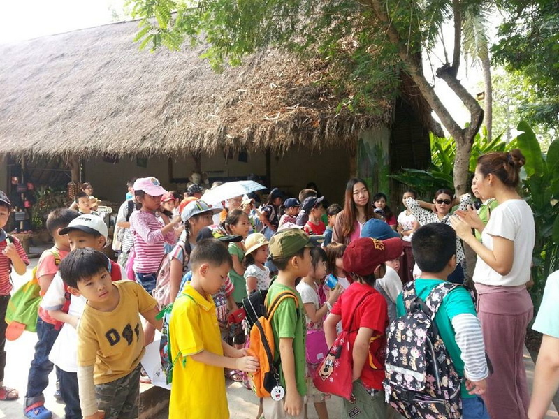 Children gathered outdoors in front of a thatched-roof building during daytime at Elephant Poopoo Paper Park.