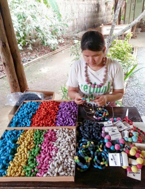 Girl Making Felt Jewelry at Elephant Poopoopaper Park Girl crafting jewelry with colorful felt balls at an outdoor table at Elephant Poopoopaper Park.