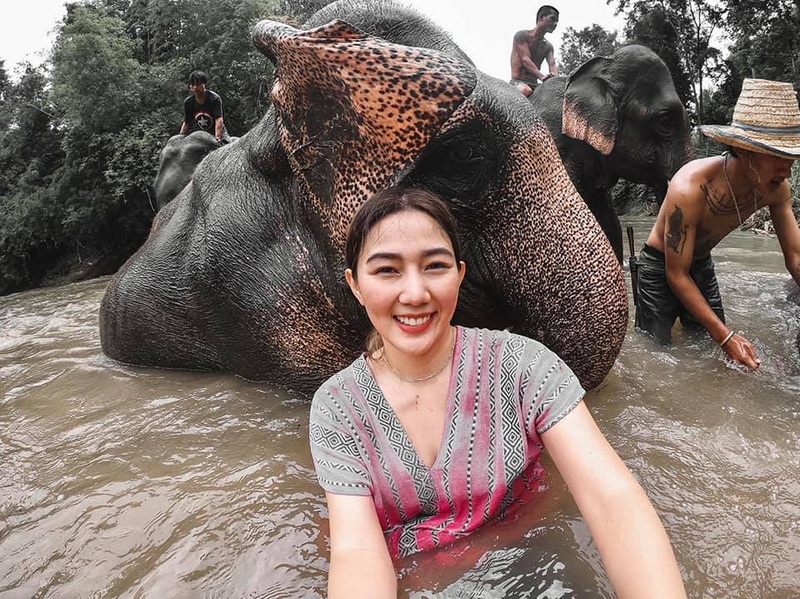 Woman sitting in water with an elephant behind her and other people nearby at Maerim Elephant Home.