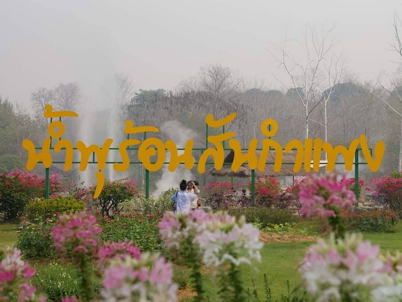 Mae Kanpong Village Hot Springs at San Kamphaeng Hot Springs People walking among blossoming flowers with steaming hot springs in the background at San Kamphaeng Hot Springs.