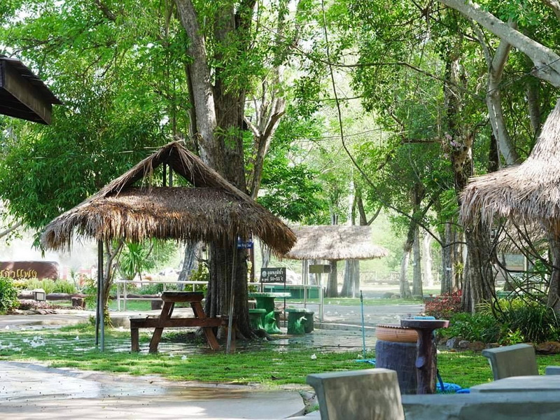 Tranquil Nature Outdoor Area at San Kamphaeng Hot Springs Thatched-roof huts and picnic tables among tall green trees in a shaded outdoor area at San Kamphaeng Hot Springs.