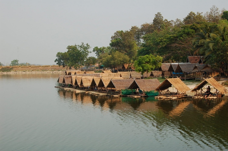 Thatched-roof huts lining a tranquil lake with trees in the background at Huay Tung Tao Chiang Mai.