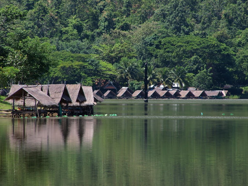 Lakeside Village Scene at Huay Tung Tao Traditional wooden huts on stilts beside a tranquil lake with green trees and hills in the background at Huay Tung Tao.
