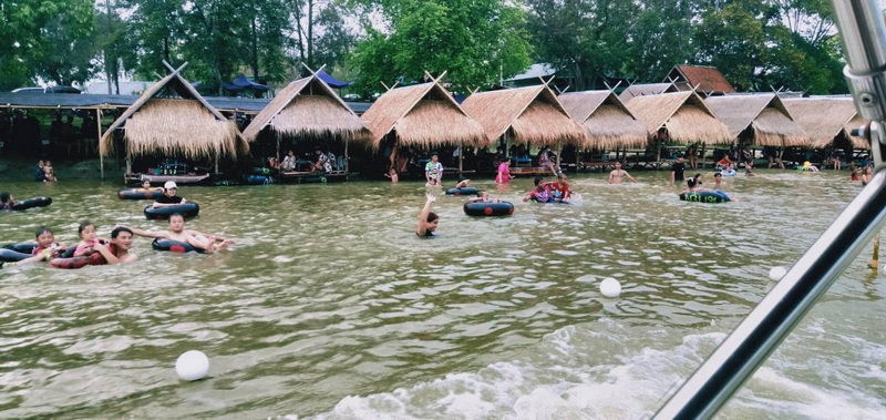 People swimming and floating in shallow water with thatched huts nearby at Huay Tung Tao Chiang Mai.