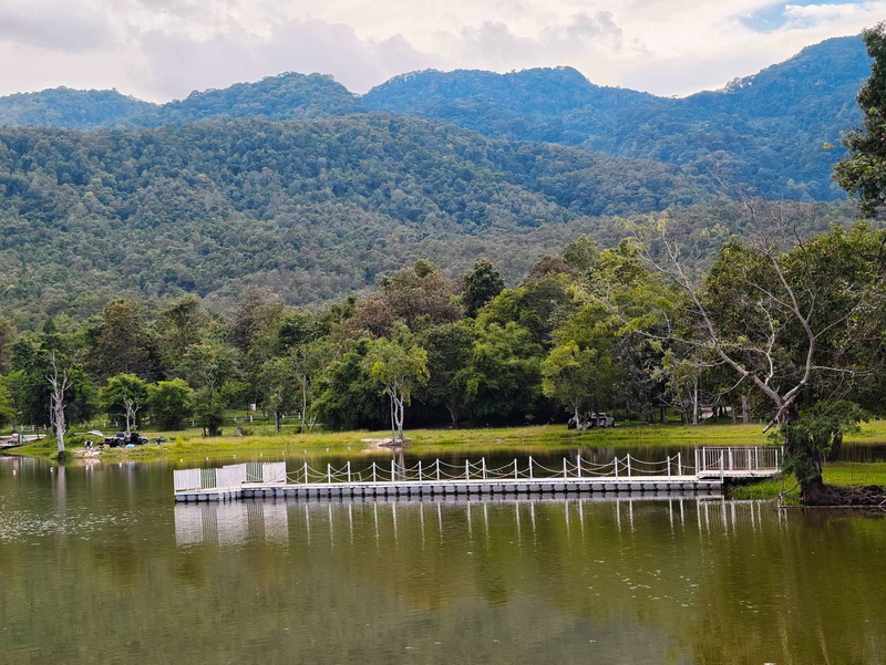 Serene lake with a wooden dock, lush greenery, and mountain backdrop at Huay Tung Tao Chiang Mai.