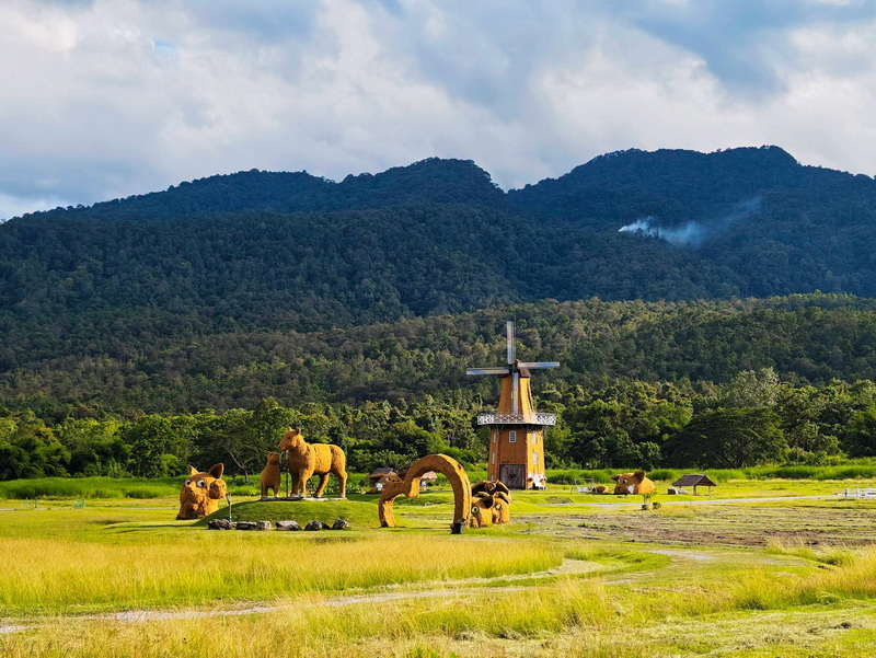 Windmill with animal sculptures on grassy plain with mountain backdrop at Huay Tung Tao.