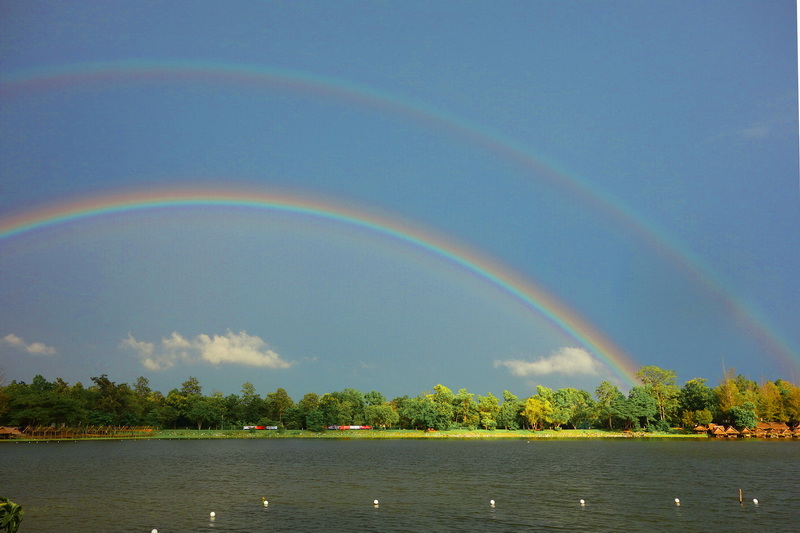 Two rainbows over a lake with green trees and a blue sky at Huay Tung Tao Chiang Mai.