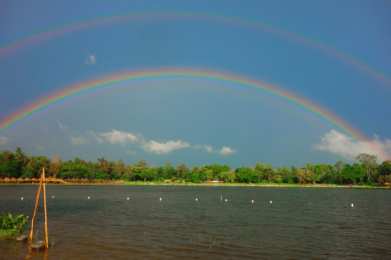 Double rainbow over a calm water body with trees along the shoreline at Huay Tung Tao Chiang Mai.