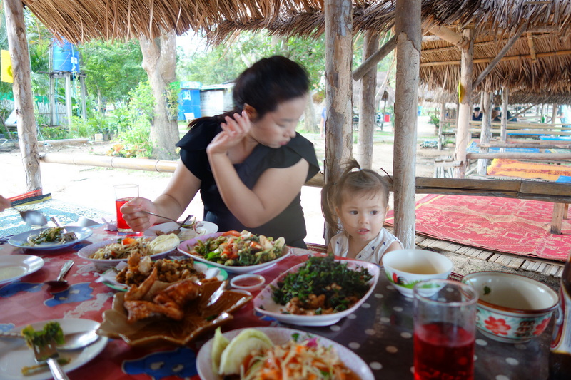 Woman and girl at a table with food under a thatched roof in outdoor setting at Huay Tung Tao.