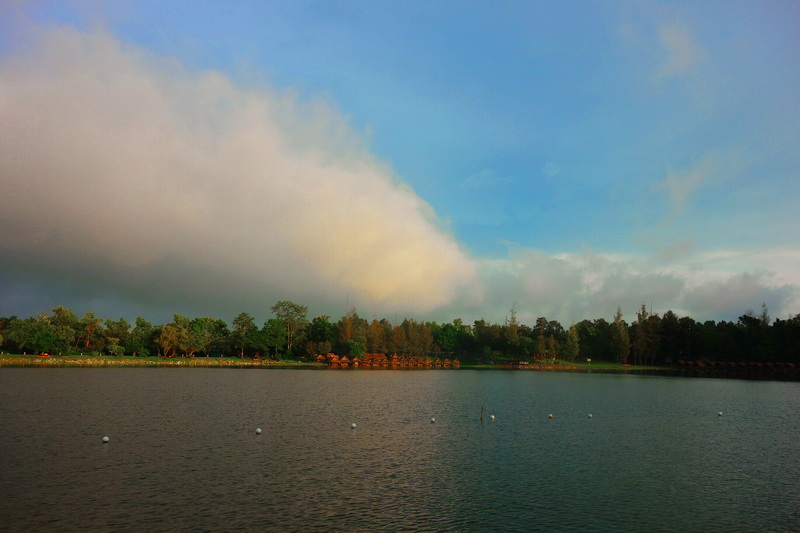 Calm lake with buoys and green trees under a partly cloudy sky at Huay Tung Tao.