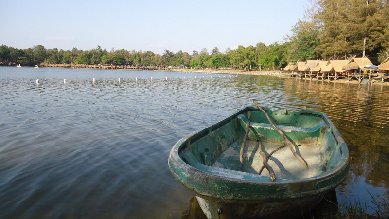 Green boat anchored on a calm lake with trees and huts in the background at Huay Tung Tao Chiang Mai.