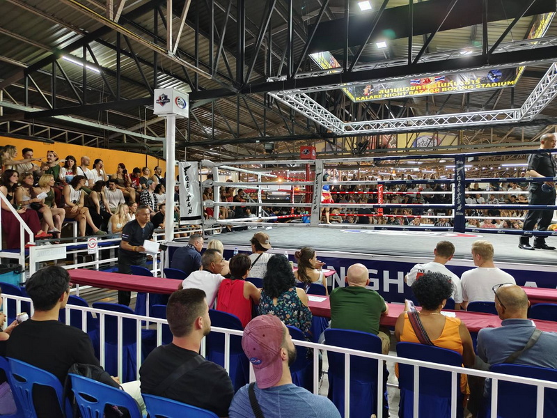 Indoor boxing event with spectators around the ring and audience seated in the arena at Kalare Boxing Stadium.