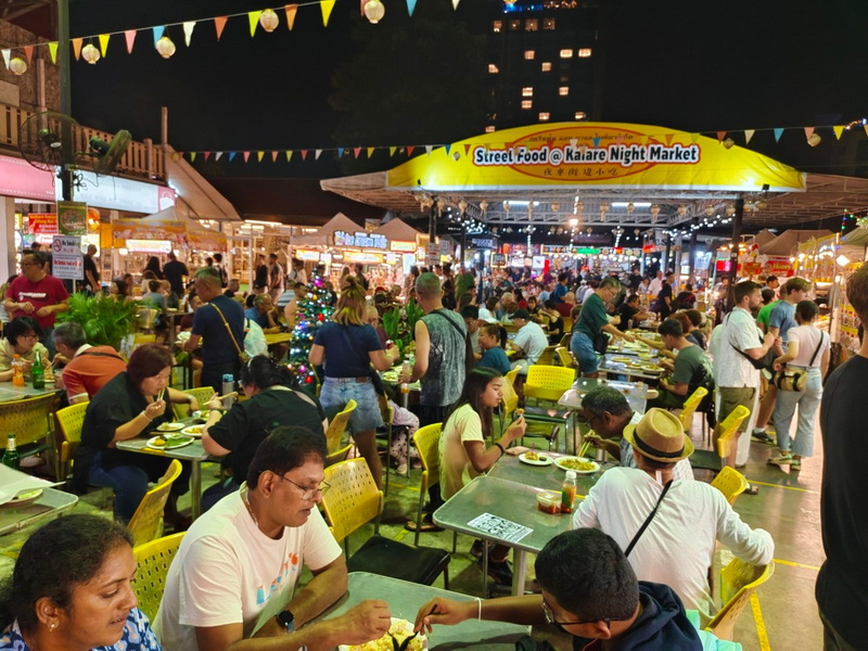 Crowded night market with people eating under string lights and food stalls in the background at Chiang Mai Night Bazaar.