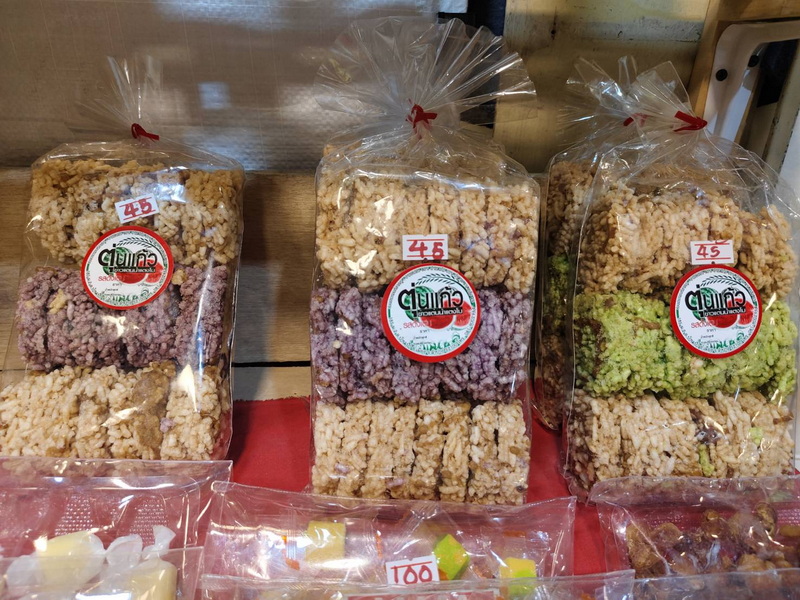 Snack Packaging Display at Top Night Markets In Chiang Mai Three bags of crunchy snack pieces with labels on a wooden surface at Top Night Markets In Chiang Mai.