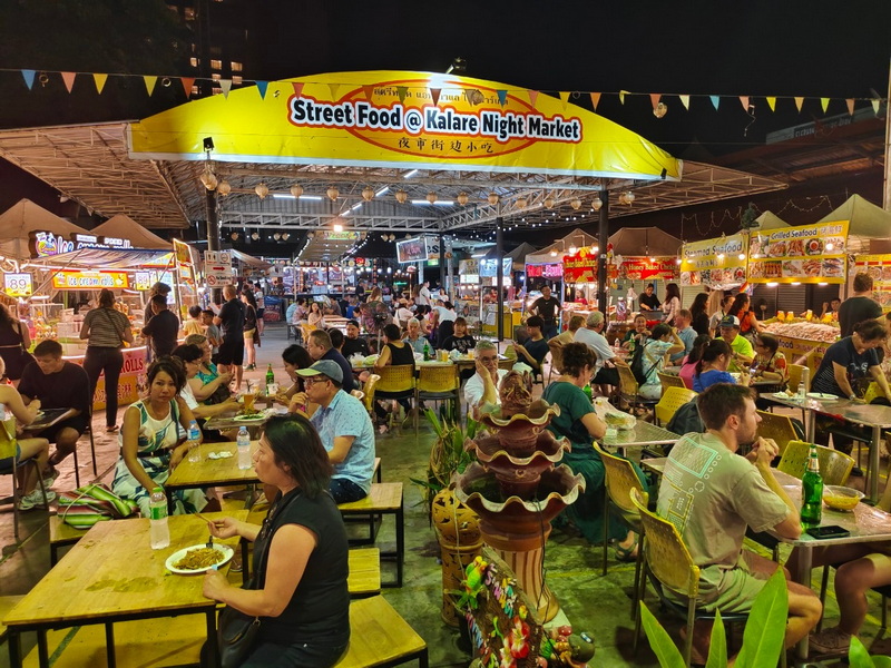 Crowded night market scene with people enjoying street food under colorful lights at Chiang Mai Night Bazaar.