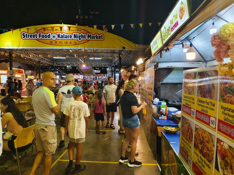 Night Market Food Scene at Best Night Markets In Chiang Mai Night market scene with food stalls, shoppers, and illuminated signs at a busy street food event at Best Night Markets In Chiang Mai.