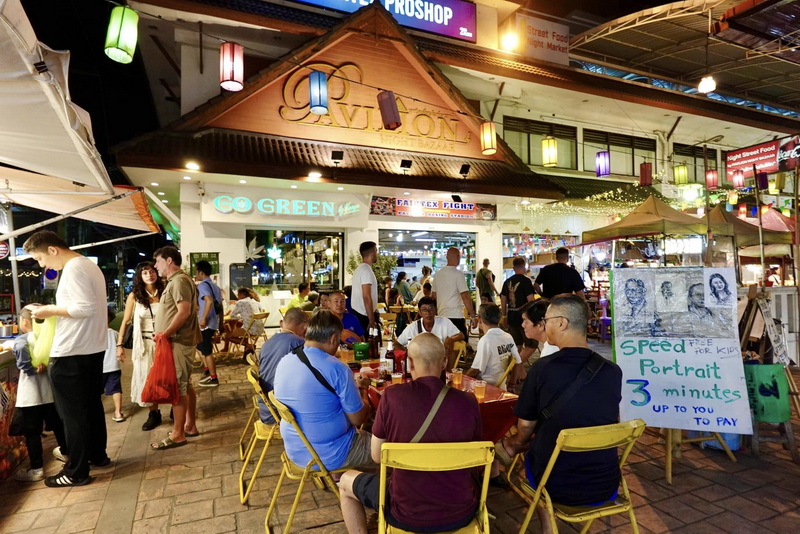 People enjoying food at a vibrant outdoor market stall with colorful lanterns at Chiang Mai Night Bazaar.