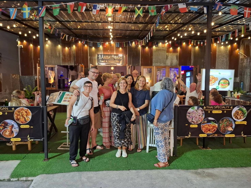 Group at Food and Music Bar at Chiang Mai Street Food Night Markets People gathered outside a food and music bar decorated with flags and string lights at Chiang Mai Street Food Night Markets.