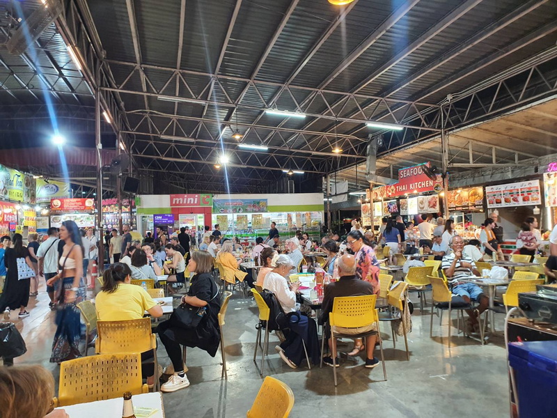 Indoor Dining at Food Market at Chiang Mai Night Market Food Guide Indoor food court with many diners and food stalls under a metal roof at Chiang Mai Night Market Food Guide.
