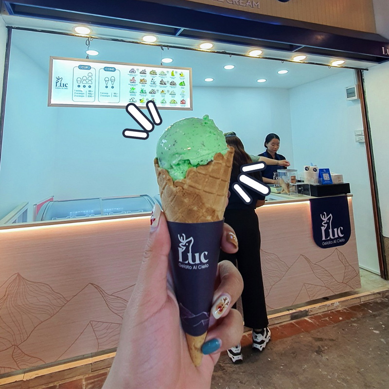 Ice Cream at a Shop at Chiang Mai Street Food Night Markets Green ice cream cone held in front of an ice cream shop with staff behind the counter at Chiang Mai Street Food Night Markets.
