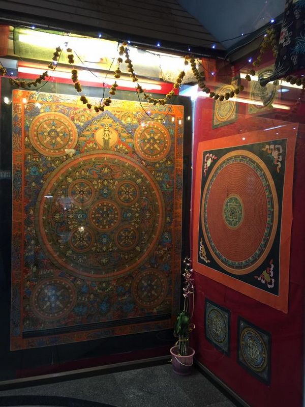 Colorful mandala artworks on glass and wall with decorative string lights inside at Chiang Mai Night Bazaar.