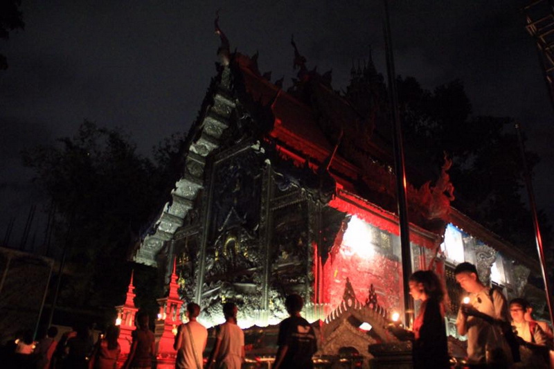 People visit a lit-up Thai temple at night with ornate designs and decorations at Saturday Night Market Chiang Mai.