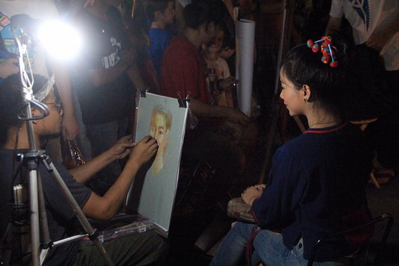 Portrait Painting Session at Saturday Walking Street Chiang Mai Artist painting a woman's portrait in a crowded indoor space at Saturday Walking Street Chiang Mai.