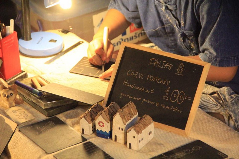 Night Writing at Market Stall at Saturday Walking Street Chiang Mai Person writing on a black notepad with small house models and postcard sign on the table at Saturday Walking Street Chiang Mai.