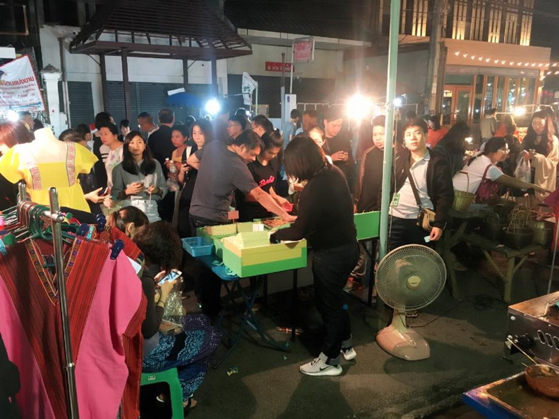 People browsing and shopping at a busy night market with bright lights and vendor stalls at Wua Lai Walking Street Chiang Mai.
