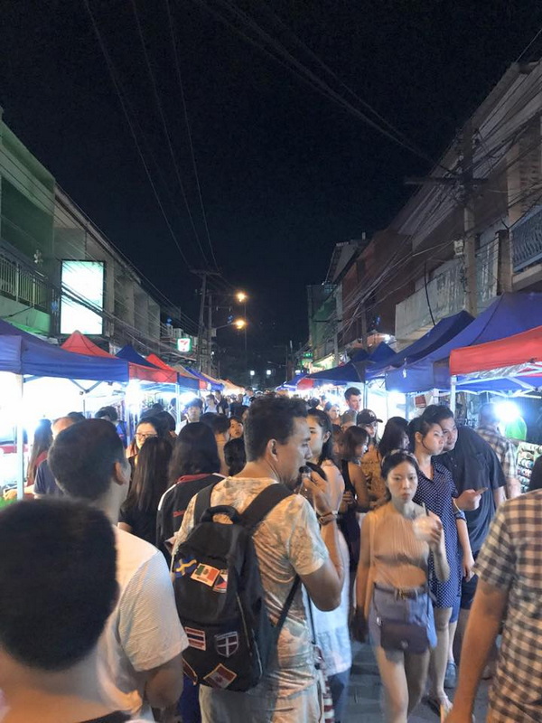 Night market with busy crowd and colorful food stalls at night at Saturday Night Market Chiang Mai.